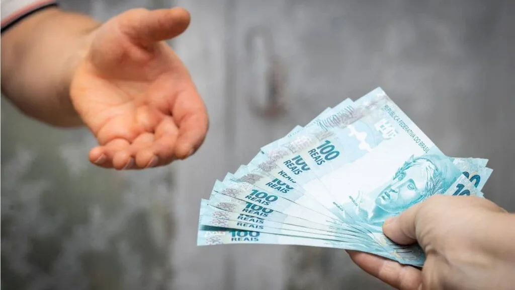 Pessoa que acabou de receber do INSS pegando seu benefício em notas de 100 reais.